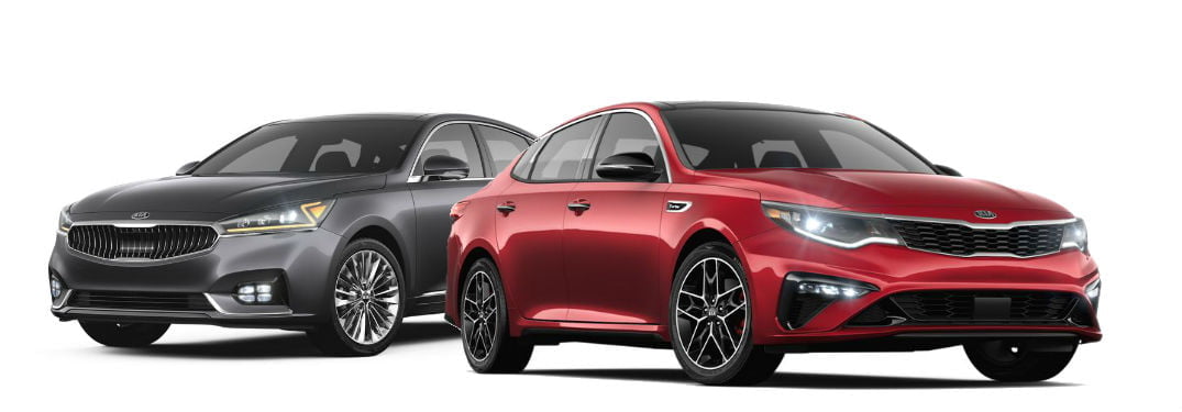 Two modern Kia sedans, one gray and one red, are parked side by side on a white background. Both cars feature sleek designs with prominent front grilles and LED headlights.