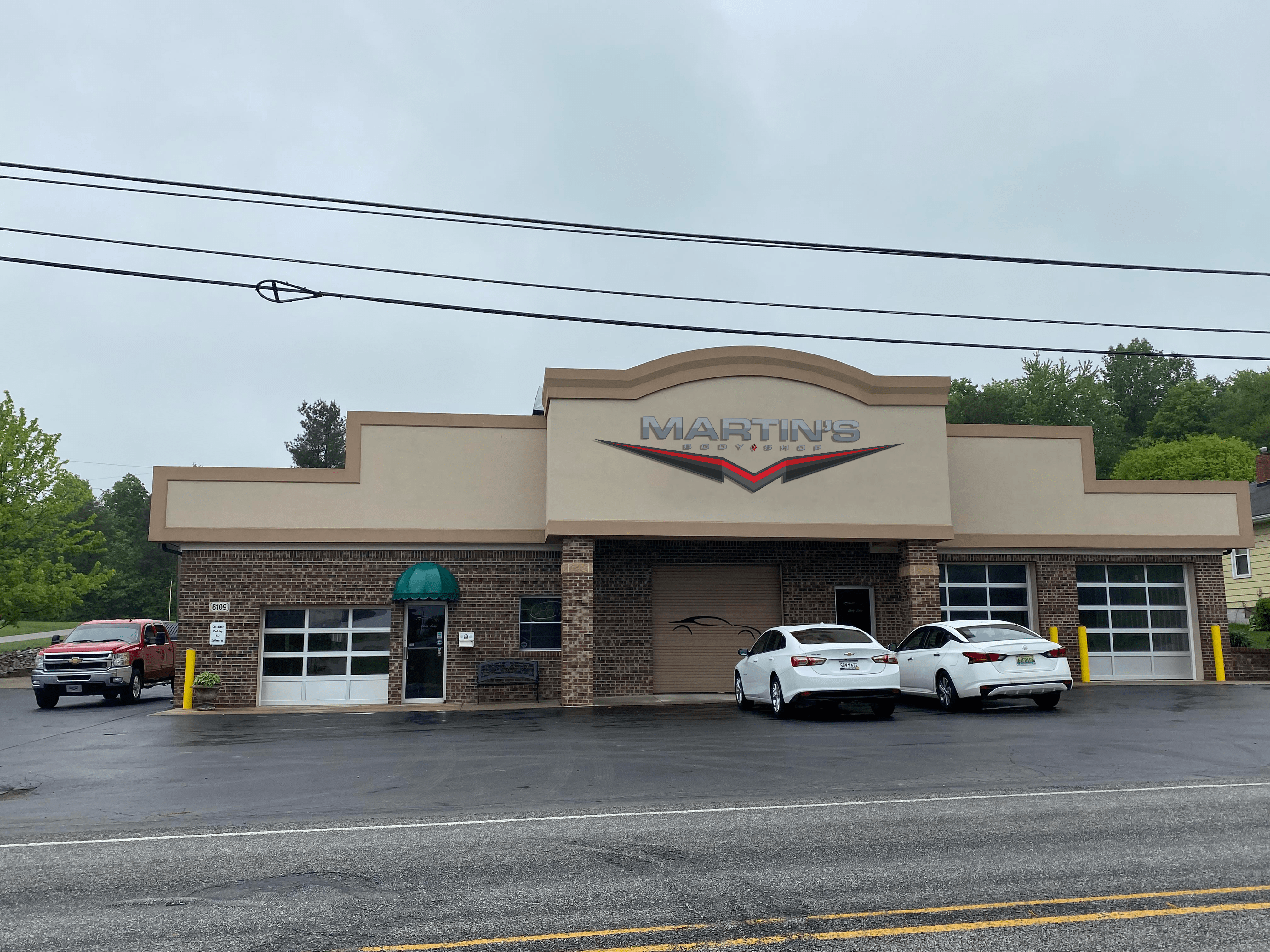 jeckers martin's sign A brick automotive service shop with a sign reading Martin’s above the entrance. Two white cars are parked by three garage bays. The sky is overcast and the building, one of several Martin’s Body Shop locations, sits by a main road.